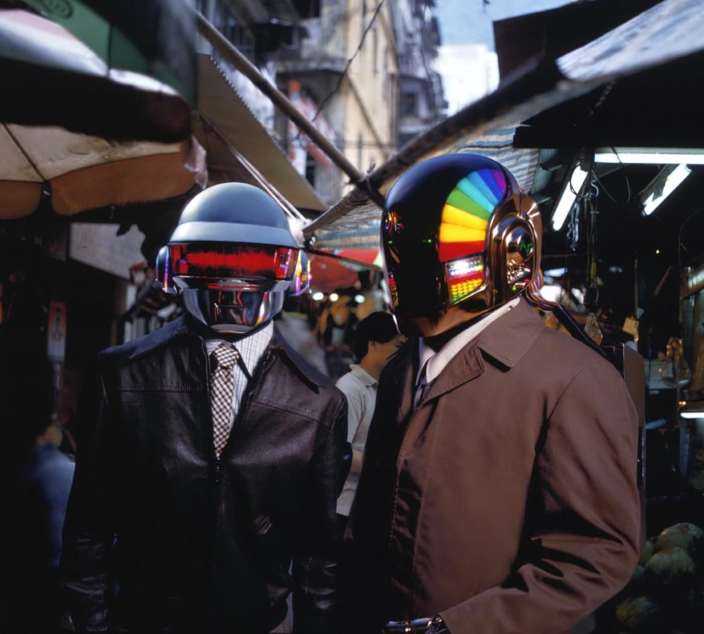 Two men in robot helmets standing in a mid shot.