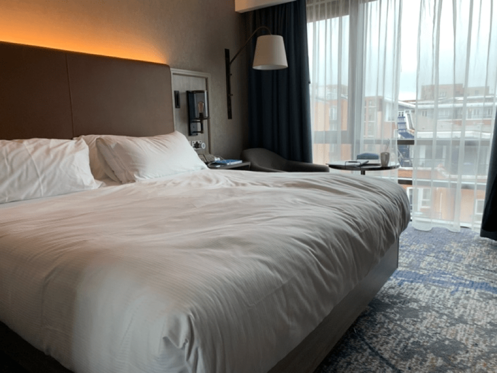 The hotel room in which one of the students is living in, fitted with a double bed and arm chair, with a view of the building opposite.