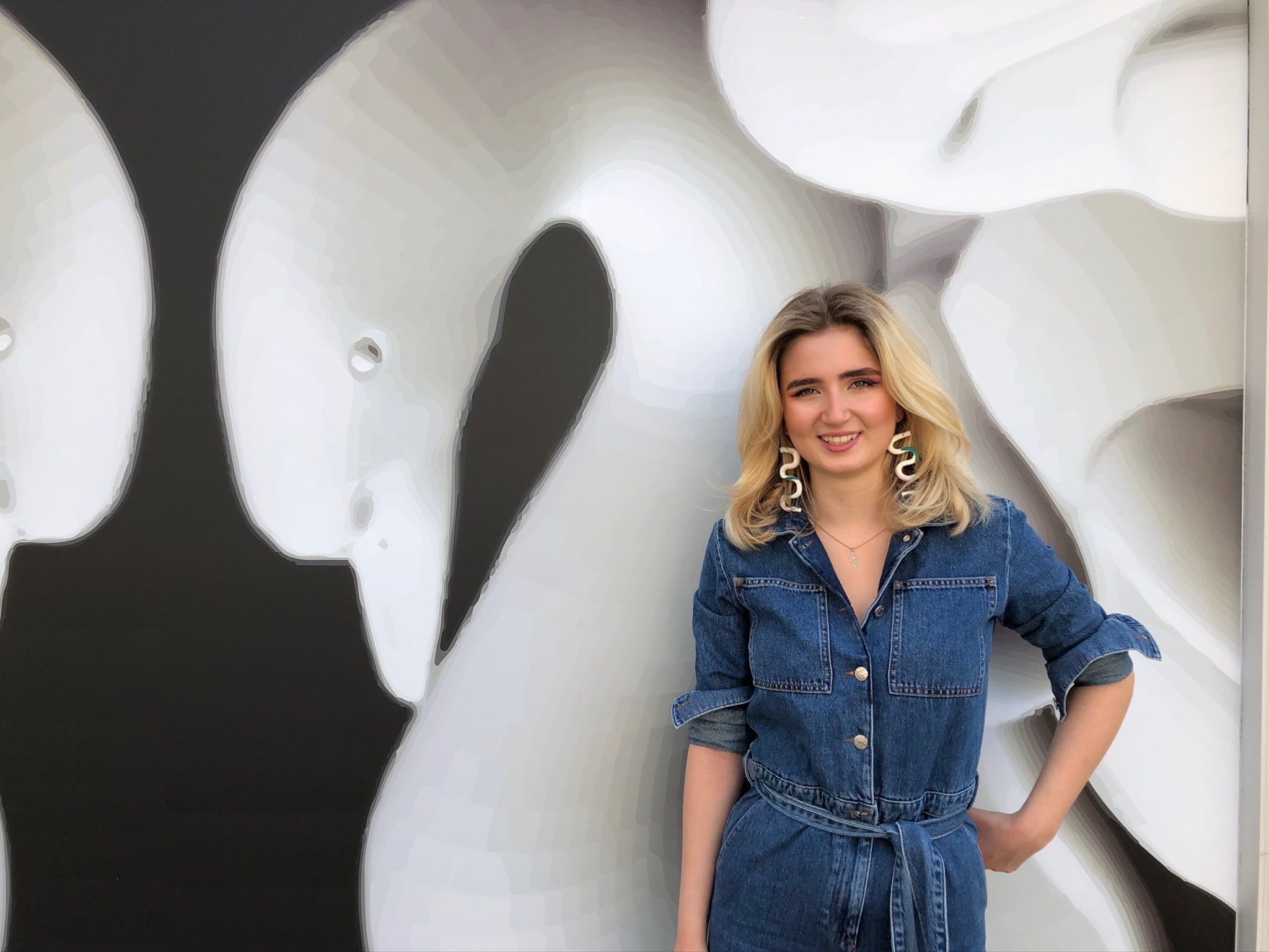 Person with blonde hair and denim dress standing in front of swam artwork