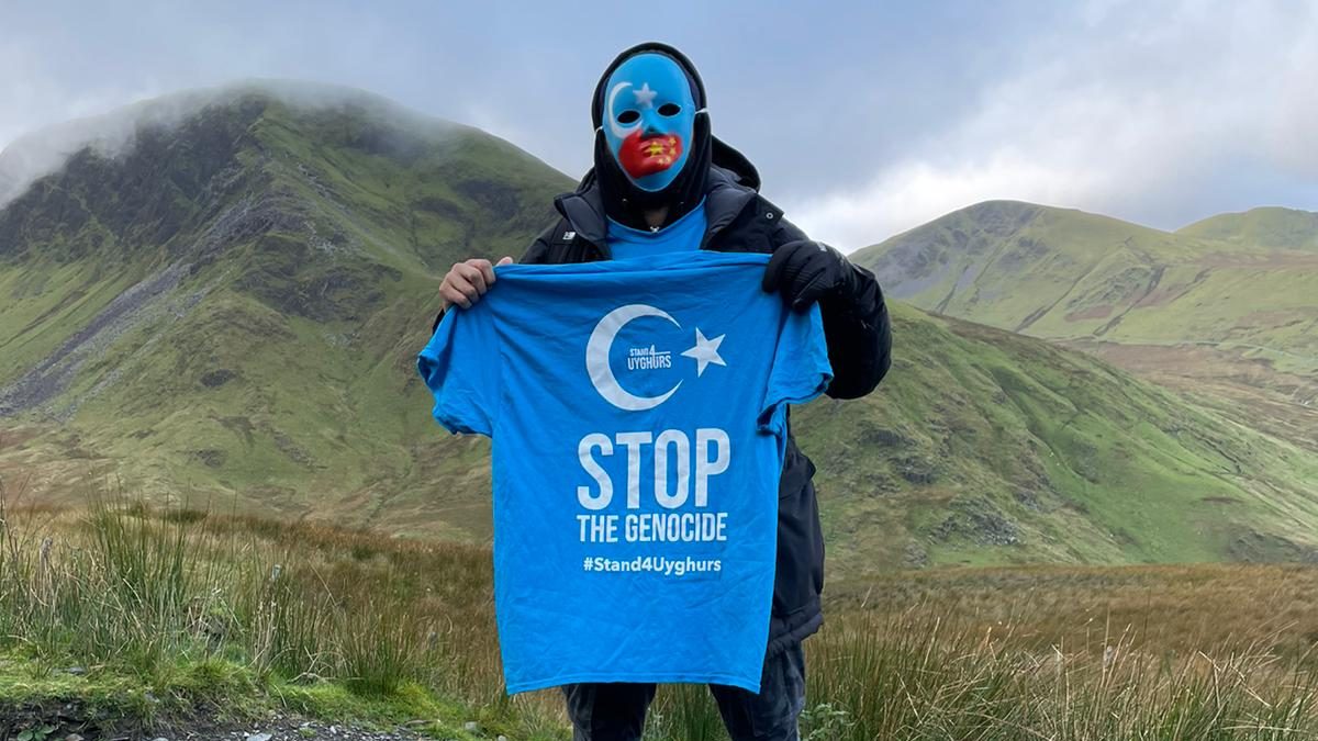 Person standing on a mountain with a blue mask holding a blue tshirt