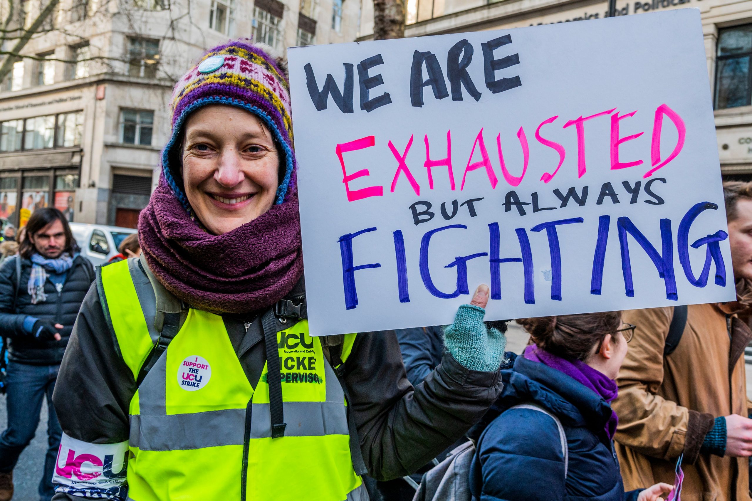 A woman holding a sign reading 'We are exhausted but always fighting'