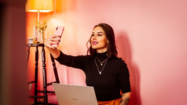 woman taking a selfie whilst holding a laptop. 