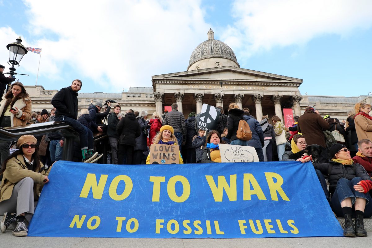 Protester outside Trafalguar Square holding a banner reading 'No to war, No to fossil fuels'
