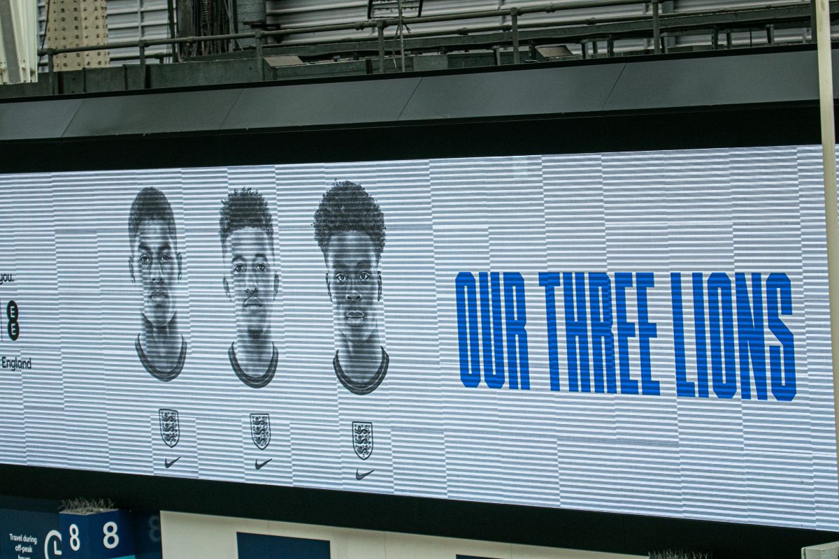 A projector at Waterloo station with the faces of Marcus Rashford, Jadon Sancho and Bukayo Saka. Next to Saka says 'Our Three Lions'.