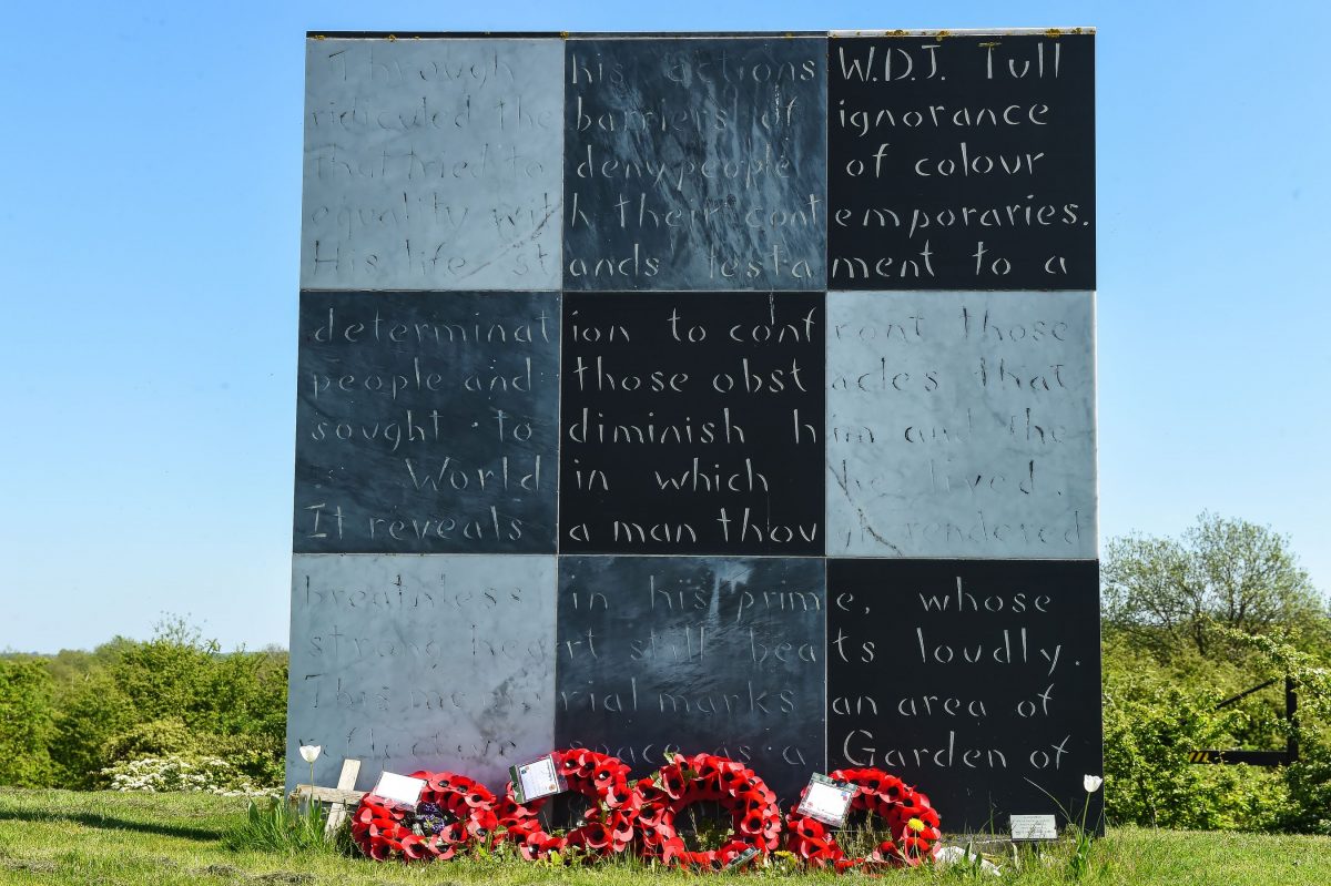 A large plaque with six squares with writing on them that celebrates Walter Tull's achievements. At the bottom of the plaque there are four red wreaths.