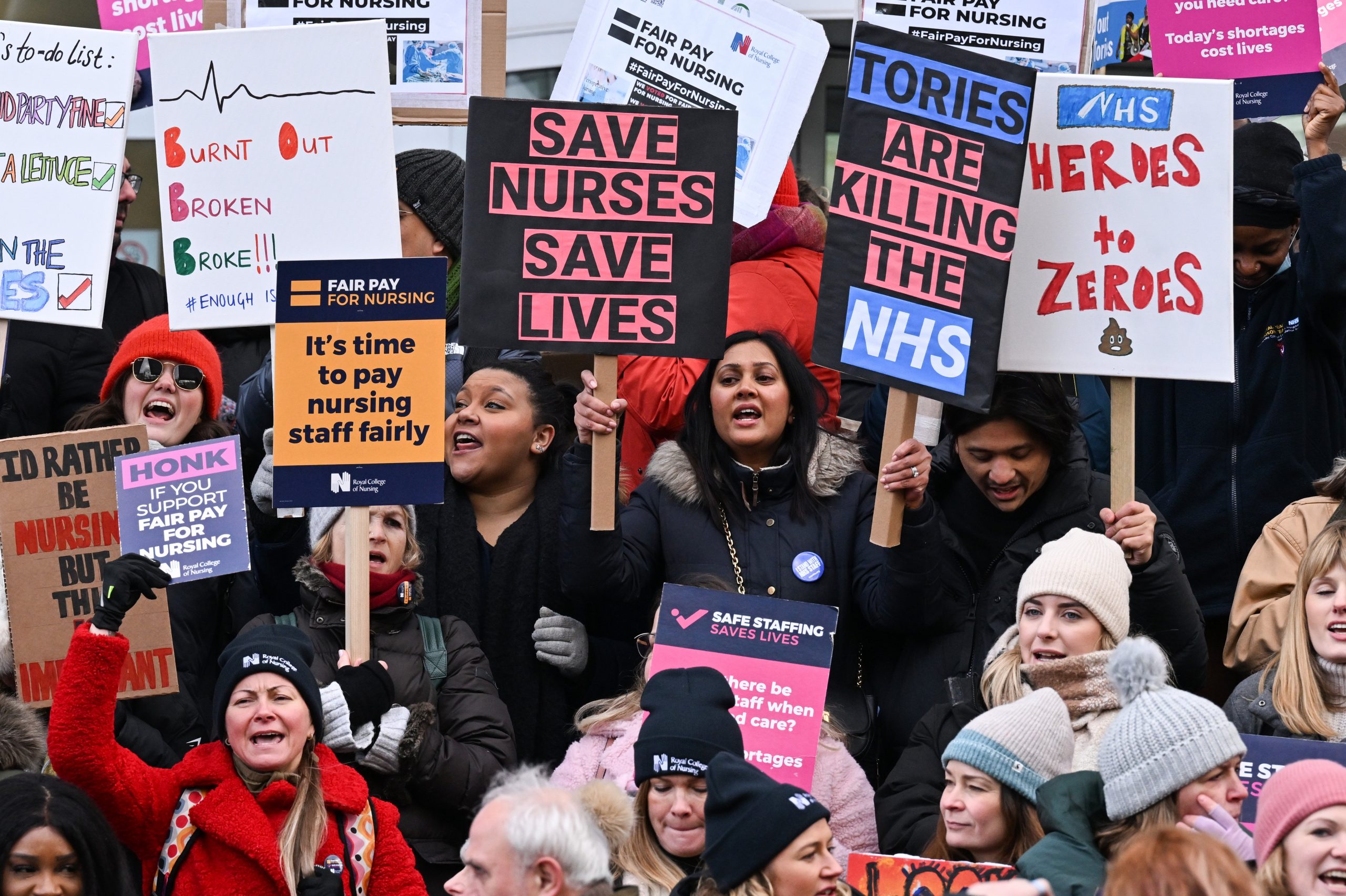 women holding picket signs with lettering such as 'save nurses save lives' another says 'tories are killing the NHS'