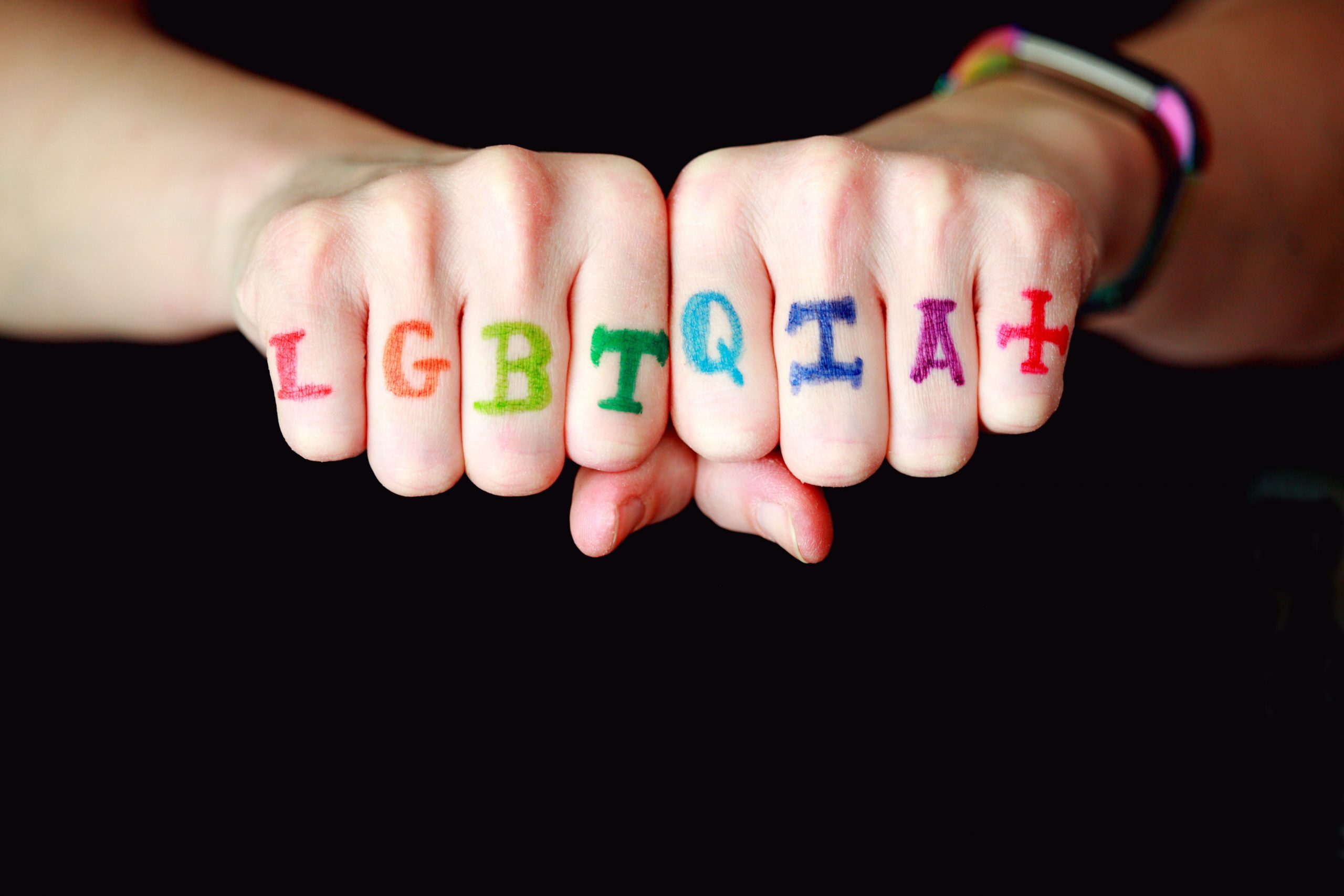 Image showing a person's knuckles which as coloured lettering: LGBTQIA+.
