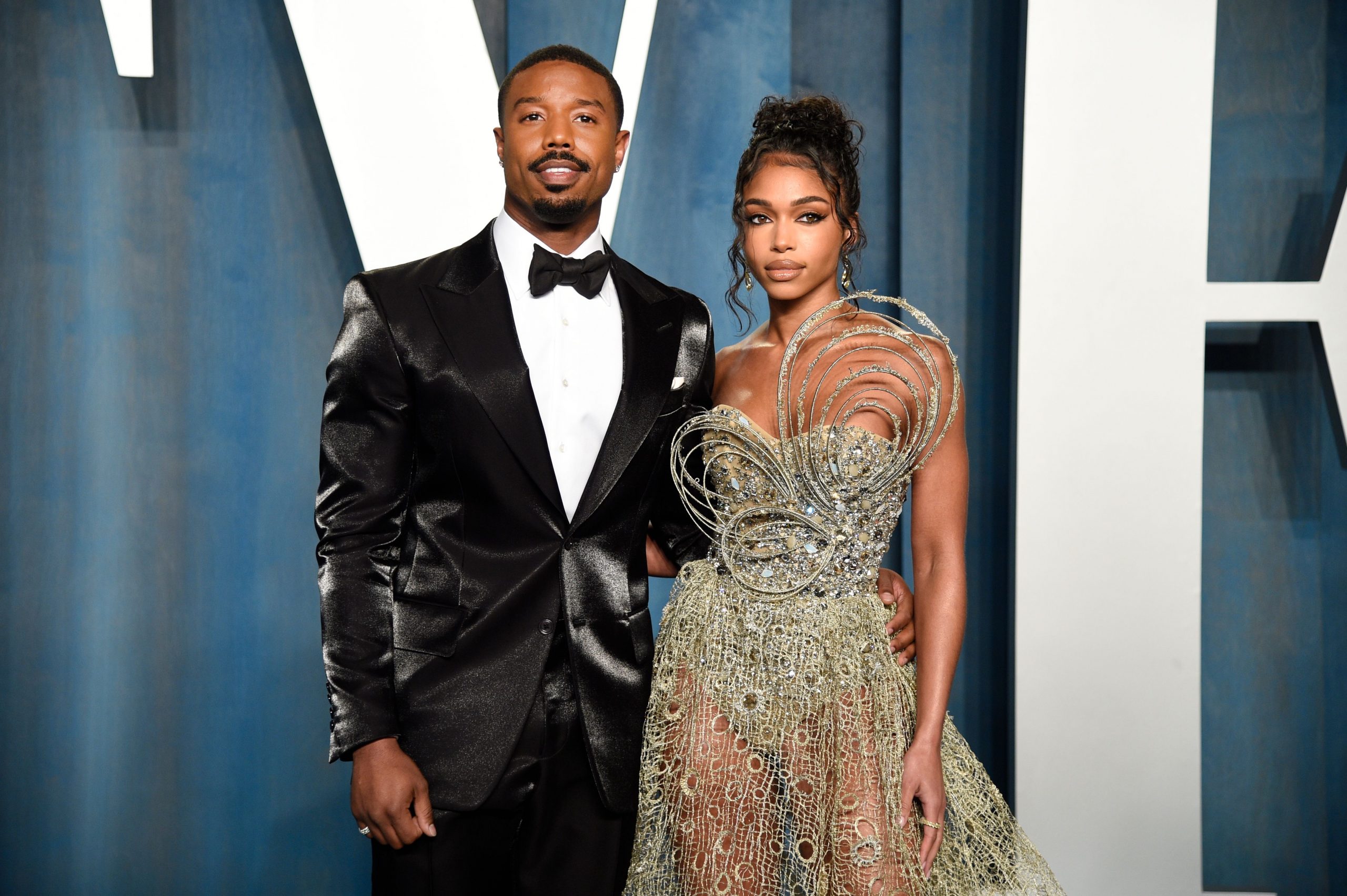 Michael B Jordan standing with Lori Harvey . Michael B Jordan is wearing a Tuxedo and Lori Harvey is wearing a gold gown.