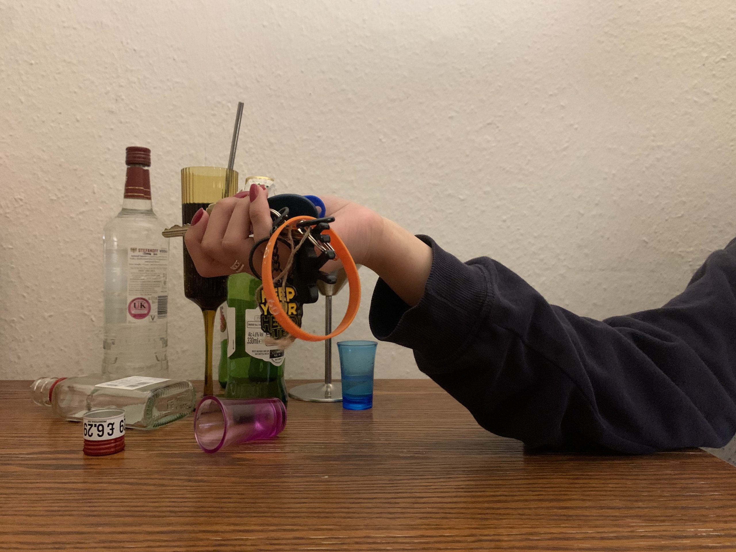A girl holding keys surrounded by alcohol bottles