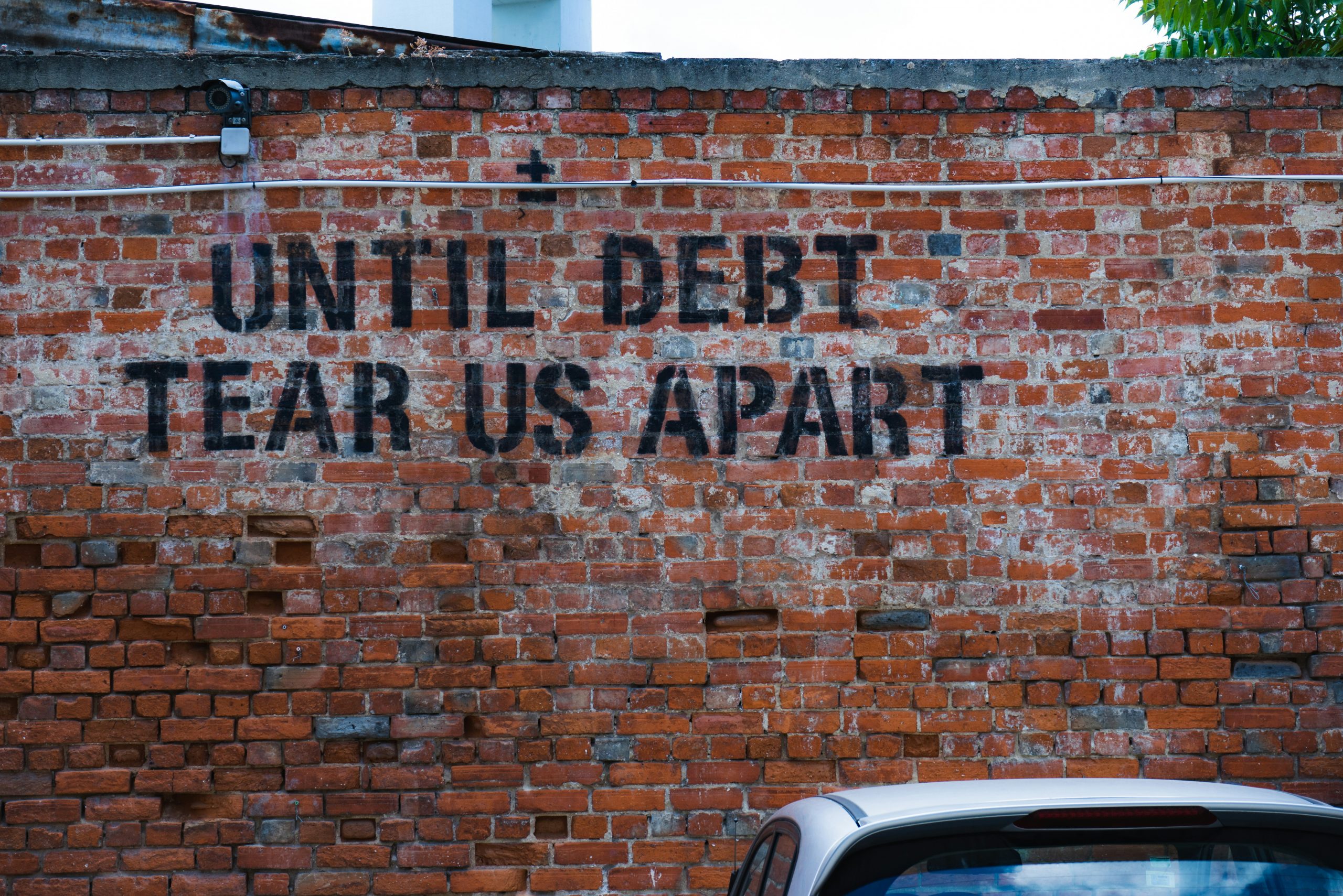 Brick wall with "Until debt tear us apart" written on it